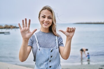 Young caucasian woman outdoors showing and pointing up with fingers number six while smiling confident and happy.