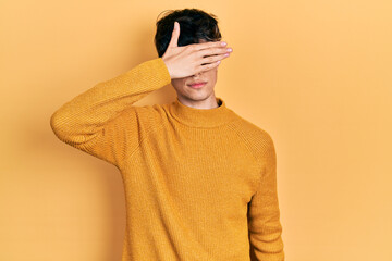 Handsome hipster young man wearing casual yellow sweater covering eyes with hand, looking serious and sad. sightless, hiding and rejection concept