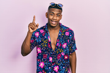 Young black man wearing hawaiian shirt and sunglasses pointing finger up with successful idea....