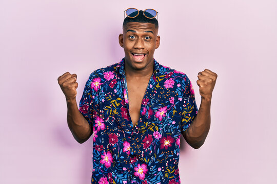 Young black man wearing hawaiian shirt and sunglasses celebrating surprised and amazed for success with arms raised and open eyes. winner concept.
