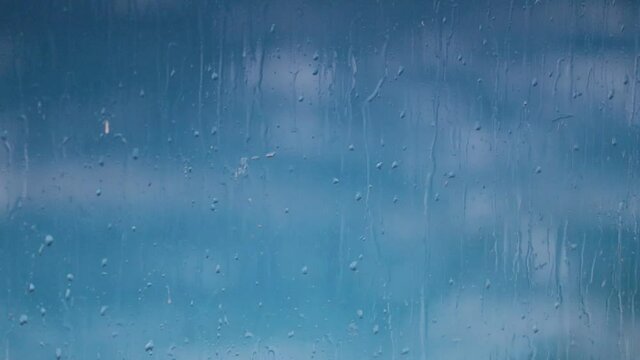 Raindrops dripping down a dirty glass pane with blue pool waves in the background 