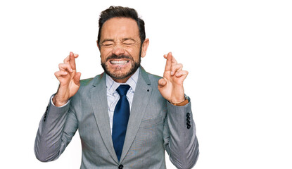 Middle age man wearing business clothes gesturing finger crossed smiling with hope and eyes closed....