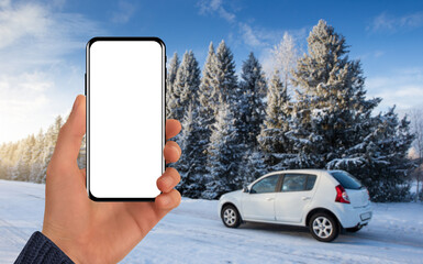 Hand with a phone on the background of a car behind a winter road. Blank screen, you can add your content