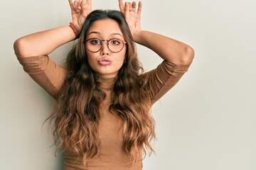 Young hispanic girl wearing casual clothes and glasses doing funny gesture with finger over head as...