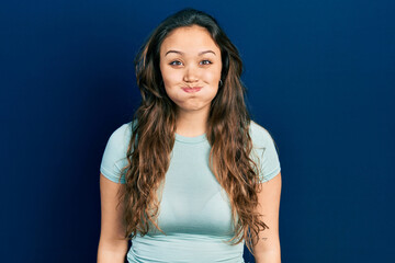 Young hispanic girl wearing casual clothes puffing cheeks with funny face. mouth inflated with air, crazy expression.