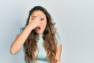 Fototapeta premium Young hispanic girl wearing casual shirt peeking in shock covering face and eyes with hand, looking through fingers afraid