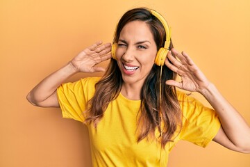 Young latin woman listening to music using headphones winking looking at the camera with sexy...