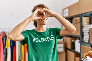 Young caucasian volunteer woman smiling happy doing heart symbol with hands over eye at charity center.