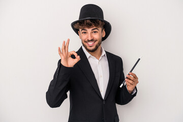 Young arab wizard man holding a wand isolated on white background cheerful and confident showing ok...