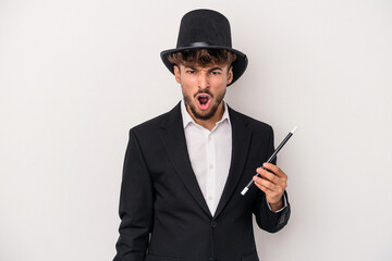 Young arab wizard man holding a wand isolated on white background screaming very angry and...