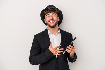 Young arab wizard man holding a wand isolated on white background laughs out loudly keeping hand on...