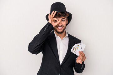 Young arab wizard man holding a magic cards isolated on white background excited keeping ok gesture...