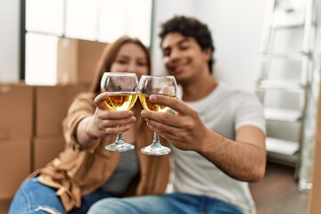 Young couple smiling happy toasting with glass of wine at new home.