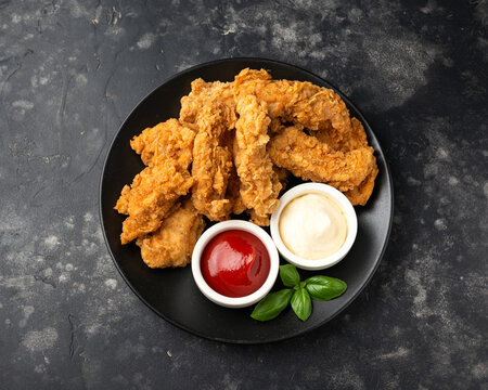 Fried Chicken strips with ketchup and mayonnaise on black plate. Fast Food