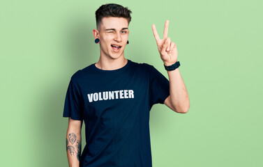 Young caucasian boy with ears dilation wearing volunteer t shirt smiling with happy face winking at...