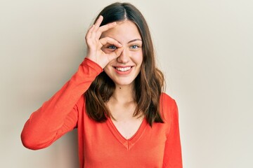 Young brunette woman wearing casual clothes doing ok gesture with hand smiling, eye looking through...