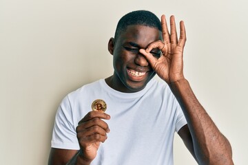 Young african american man holding virtual currency bitcoin smiling happy doing ok sign with hand...