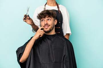 Young arab man ready to get a haircut isolated on blue background relaxed thinking about something looking at a copy space.