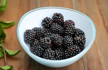 Eine Schale mit reifen und gewaschenen Brombeeren auf einem Holztisch.
