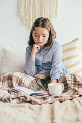 Obraz na płótnie Canvas Young girl holding cozy mug with cacao or chocolate, reading book. Cozy home, winter mood concept