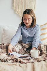 Young girl holding cozy mug with cacao or chocolate, reading book. Cozy home, winter mood concept