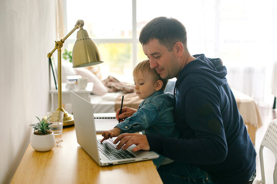 Business Man Working At Home With Laptop With A Baby Son On His Hands.