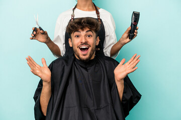 Young arab man ready to get a haircut isolated on blue background receiving a pleasant surprise,...