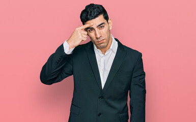 Handsome hispanic man wearing business clothes pointing unhappy to pimple on forehead, ugly infection of blackhead. acne and skin problem