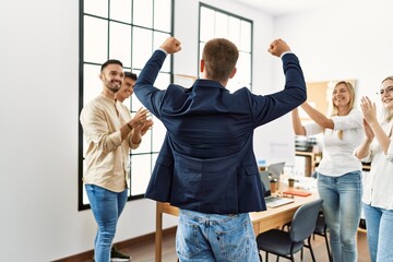 Group of young business workers smiling and clapping. Young businessman doing strong gesture with...