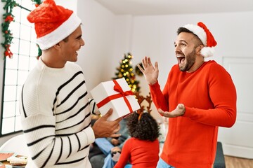 Obraz premium Group of young people on christmas meeting. Man surprising with gift to other guy at home.