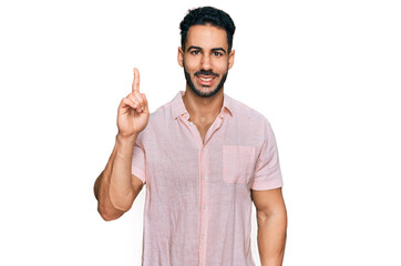 Fototapeta premium Hispanic man with beard wearing casual shirt showing and pointing up with finger number one while smiling confident and happy.