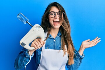 Young caucasian woman holding pastry blender electric mixer celebrating achievement with happy...