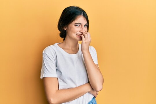 Young caucasian woman wearing casual white t shirt looking stressed and nervous with hands on mouth biting nails. anxiety problem.