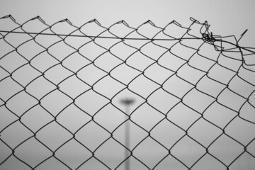 Metallic grid fence with blurry background and a streetlight in the center on a cloudy day