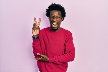 Young african american man wearing casual clothes smiling with happy face winking at the camera doing victory sign with fingers. number two.