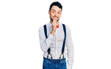 Fototapeta premium Hispanic man with beard wearing hipster look with bow tie and suspenders looking confident at the camera with smile with crossed arms and hand raised on chin. thinking positive.