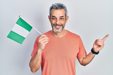 Handsome middle age man with grey hair holding nigeria flag smiling happy pointing with hand and...