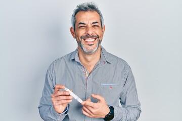 Handsome middle age man with grey hair holding glucometer device smiling and laughing hard out loud...