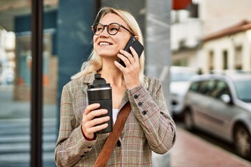 Young blonde businesswoman talking on the smartphone drinking coffee at the city.