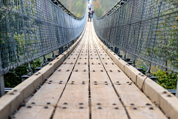 Suspension wooden bridge with steel ropes over a dense forest in West Germany, close up on a wooden walkway.