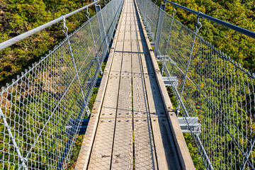 Suspension wooden bridge with steel ropes over a dense forest in West Germany, close up on a wooden walkway.