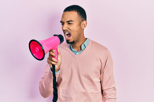 Young african american man shouthing and screaming through megaphone over pink isolated background
