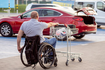 Obraz premium Person with a physical disability pushes a cart towards a car in a supermarket parking lot