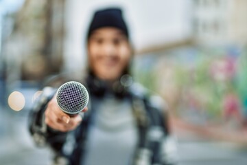 Young hispanic woman smiling happy using headphones and microphone at the city.