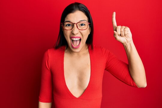 Young latin woman wearing casual clothes and glasses pointing finger up with successful idea. exited and happy. number one.