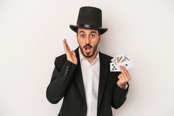 Young magician man holding a magic card isolated on white background surprised and shocked.