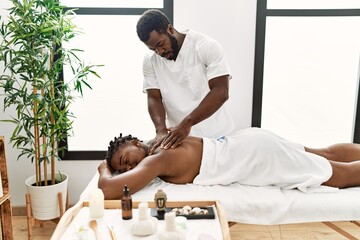 Obraz na płótnie Canvas Young physiotherapist man concentrated giving back massage to african american woman at the clinic.