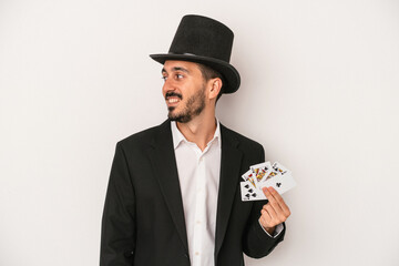 Young magician man holding a magic card isolated on white background looks aside smiling, cheerful and pleasant.