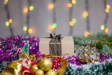 Christmas box with a gift decorated with tinsel and toys in a cold tone and against the background of a sparkling garland.