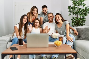 Obraz premium Group of young friends having video call using laptop sitting on the sofa at home.
